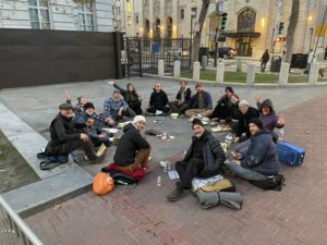 Participants in a street retreat sitting in a circle on a sidewalk